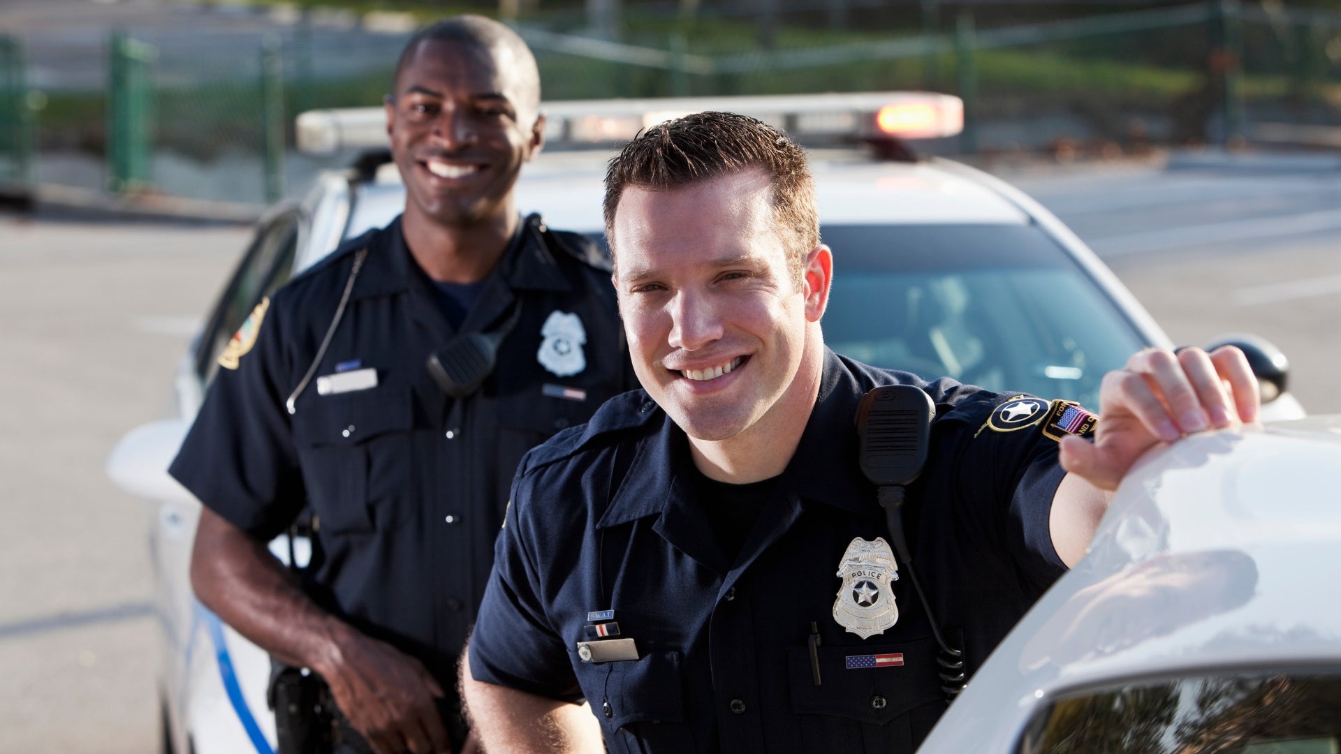 2 police officers smiling with police car in background