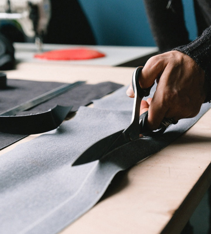 Person cutting fabric with scissors on a workbench.